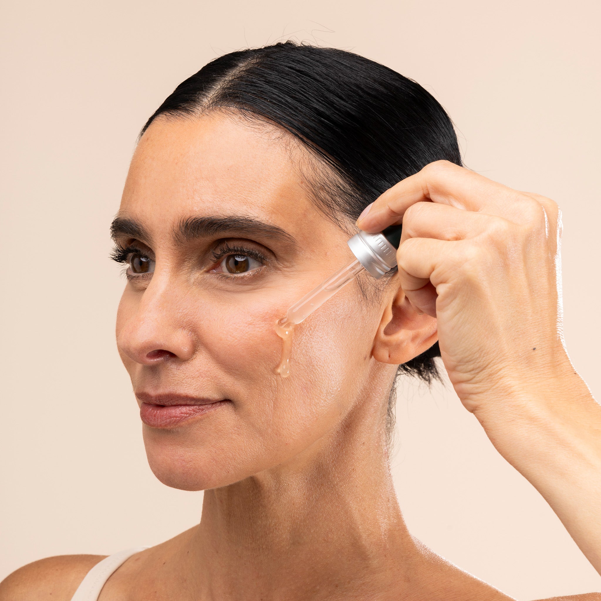 Woman applying Edelweiss Serum to her face with a dropper on a beige background