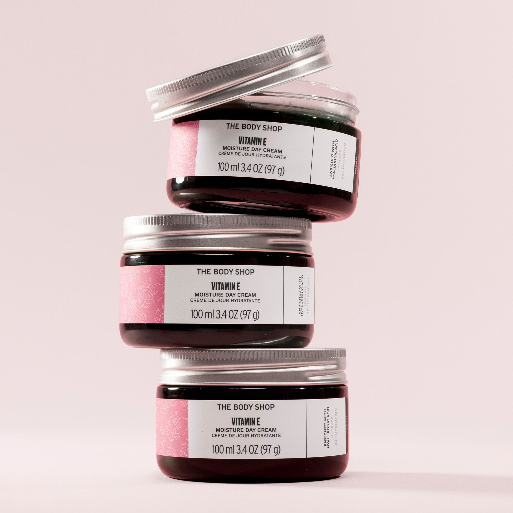 Three jars of The Body Shop Vitamin E Moisture Day Cream stacked on a light pink background